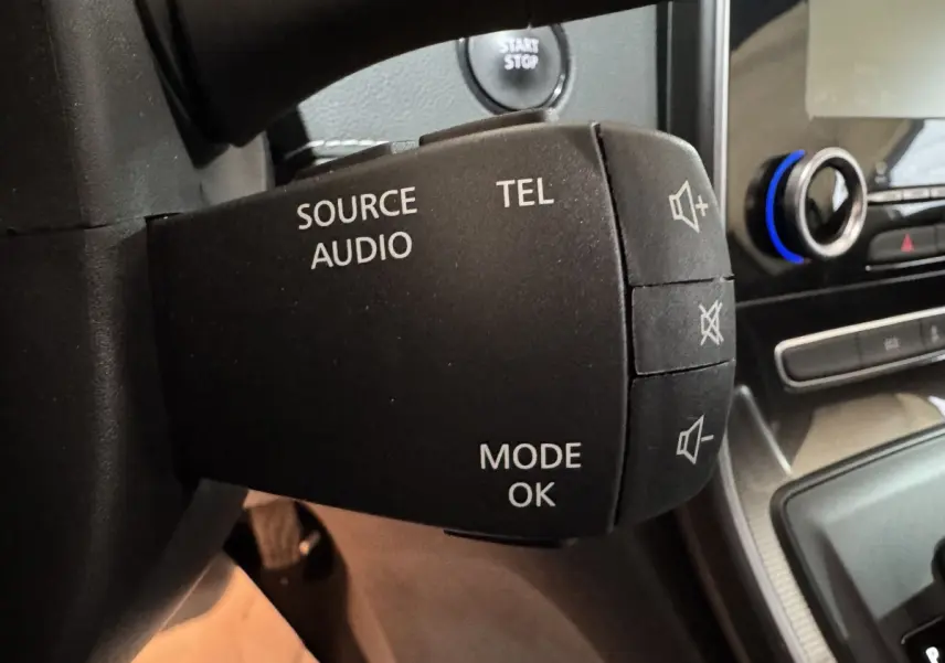Gros plan sur la commande audio au volant du Renault Scénic Intens rouge 2021, avec bouton démarrage visible en arrière-plan.
