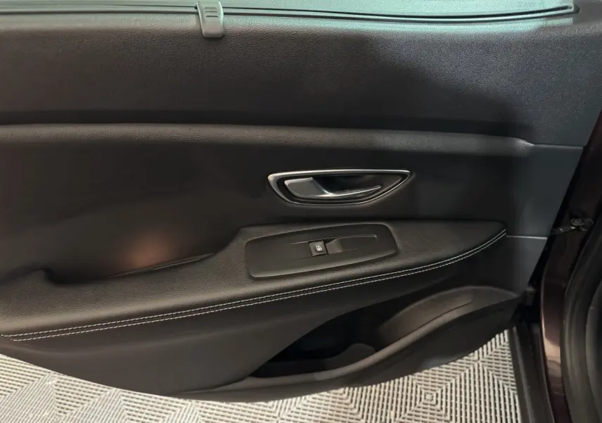 Gros plan sur la porte intérieure côté droit du Renault Scénic Intens rouge, avec poignée argentée et commande de vitre noire.