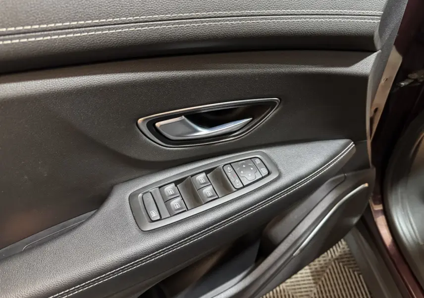 Gros plan sur la porte avant gauche du Renault Scénic Intens rouge, avec commandes des vitres et poignée argentée.