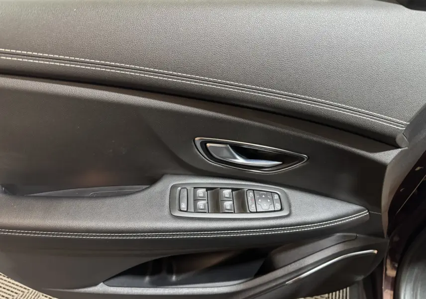 Gros plan sur la porte intérieure côté conducteur du Renault Scenic Intens rouge, avec commandes électriques et surpiqûres blanches.