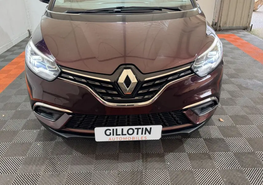 Vue frontale rapprochée du Renault Scénic Intens rouge 2021 avec phares LED allumés et calandre chromée.