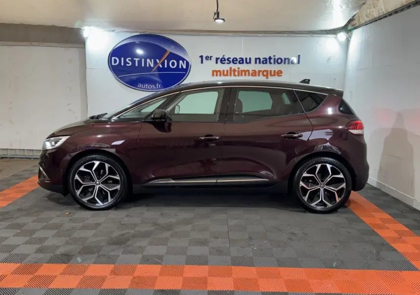 Profil droit d'un Renault Scénic Intens rouge foncé 2021 avec jantes alliage et vitres teintées en intérieur showroom.