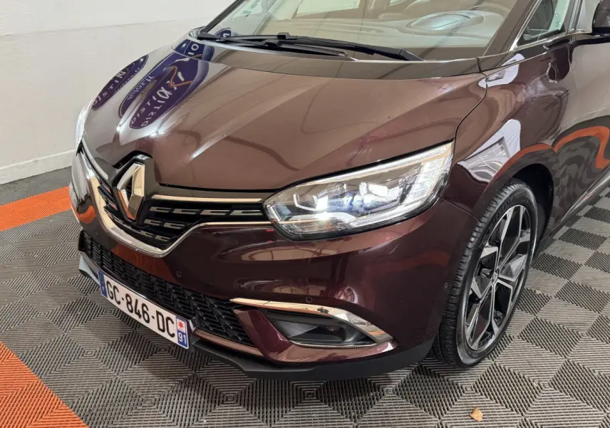 Vue 3/4 avant droit d'un Renault Scénic Intens rouge avec phares LED allumés et jantes alliage noires.