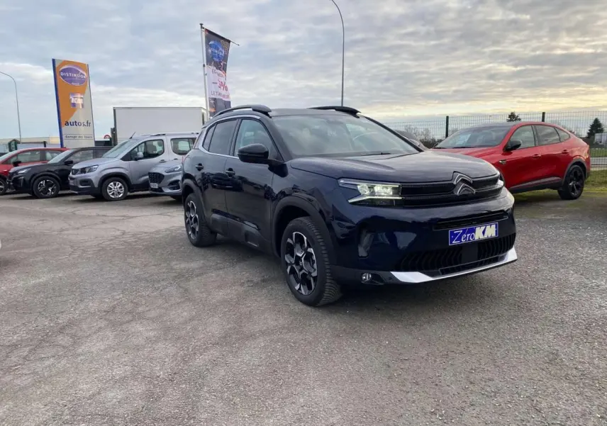 Citroën C5 Aircross bleu Eclipse en 3/4 avant droit sur parking avec autres véhicules en arrière-plan.