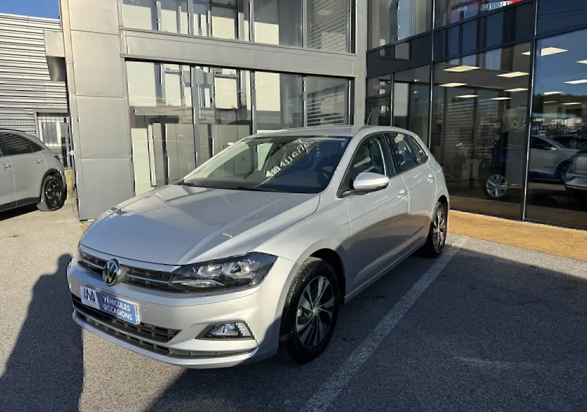 Volkswagen Polo gris métal vue 3/4 avant droit, avec jantes alliage et calandre noire brillante.