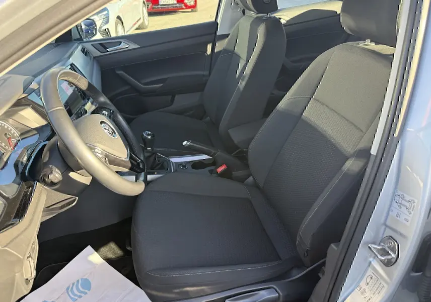 Vue intérieure côté conducteur de la Volkswagen Polo gris métal 2021, montrant les sièges noirs et la boîte manuelle.