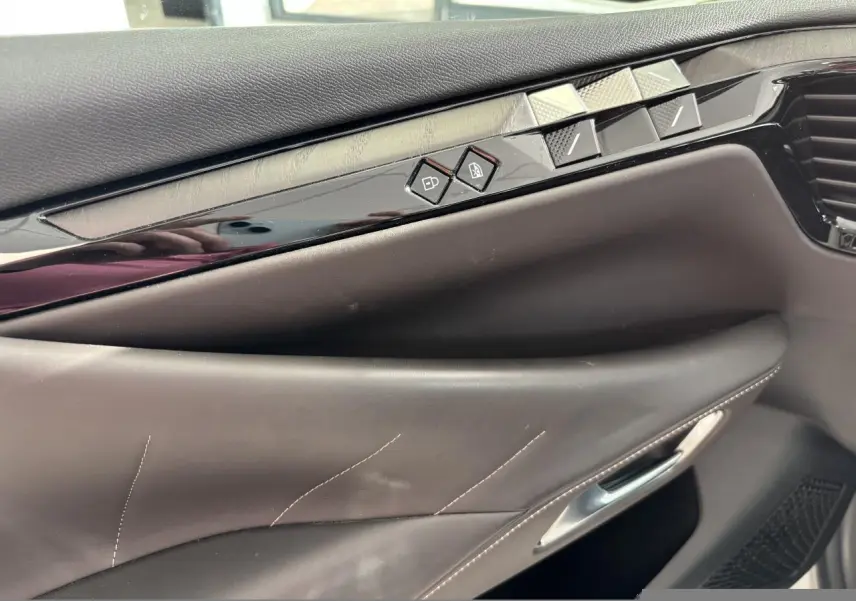 Détail de la porte avant droite du DS4 2023, cuir brun Criollo avec boutons de commande et insert noir brillant.