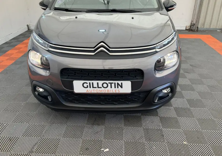 Vue avant d'une Citroën C3 gris foncé avec phares LED et calandre noire distinctive sur sol damier.