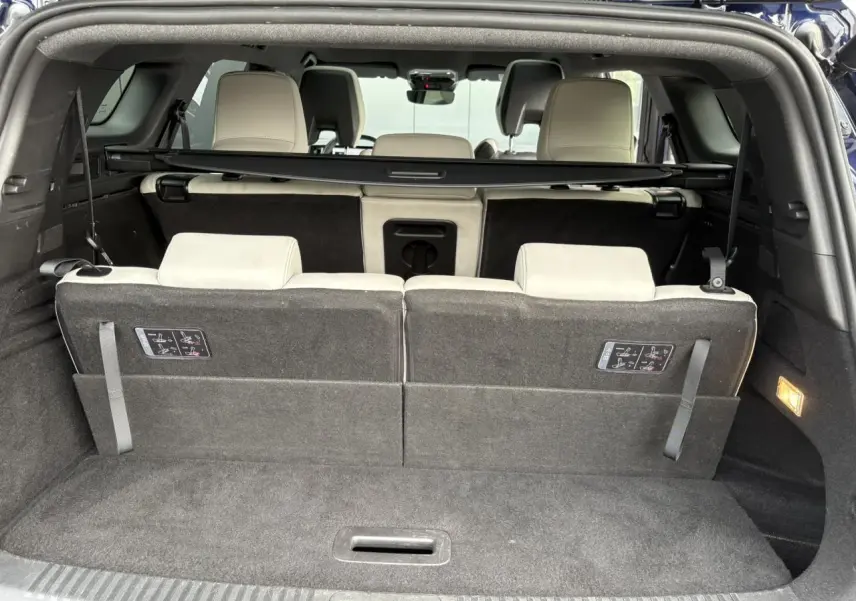 Coffre ouvert du Renault Espace VI bleu nuit montrant la troisième rangée de sièges beige clair rabattus partiellement.