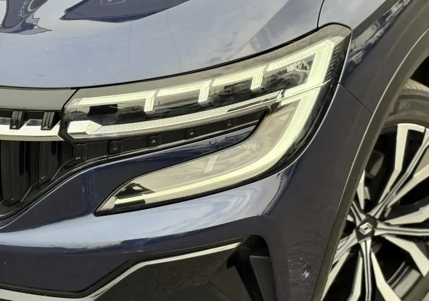 Gros plan sur le phare avant droit et la jante diamantée du Renault Espace VI Bleu Nuit avec détails lumineux LED distinctifs.