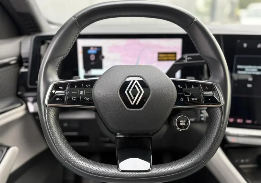 Volant cuir noir perforé avec logo Renault au centre, tableau de bord numérique et écran tactile en arrière-plan dans un Renault Espace VI 2023.