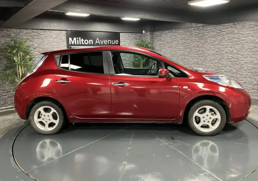Profil côté gauche d'une Nissan Leaf 30 Visia rouge métallisée de 2017, stationnée en intérieur sur plateau tournant.