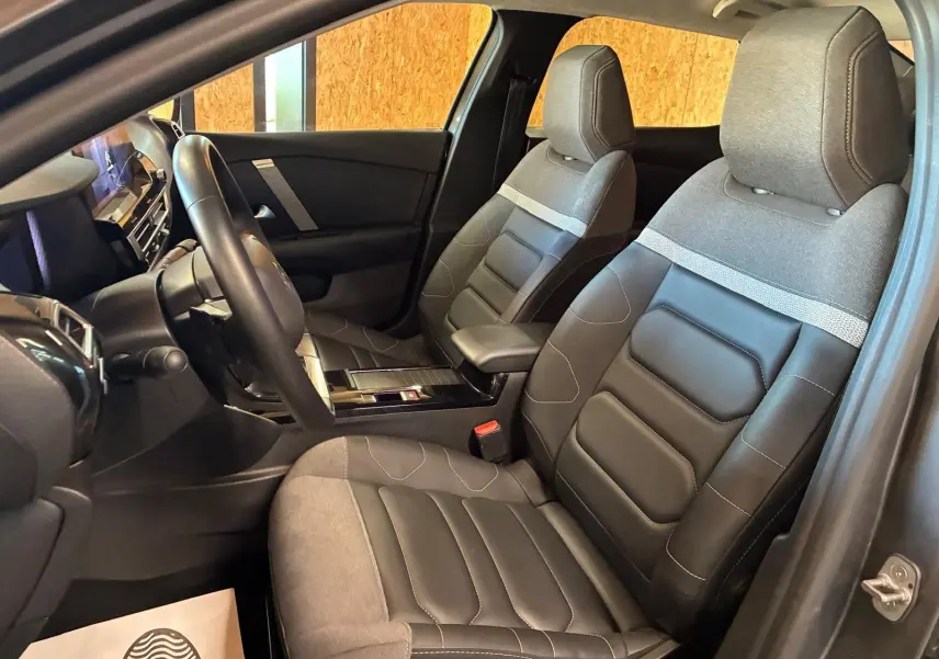 Vue intérieure côté conducteur du Citroën C4 X 2024, sièges tissu gris et cuir noir avec console centrale moderne.