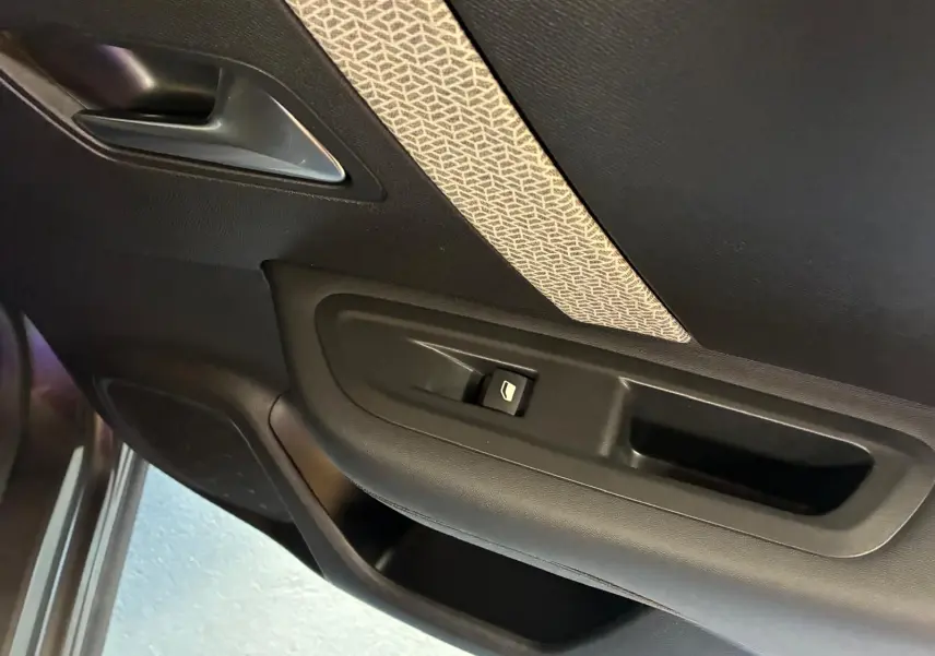 Détail de la porte intérieure côté gauche de la Citroën C4 X 2024, avec bouton de commande de vitre et insert tissu gris à motifs.