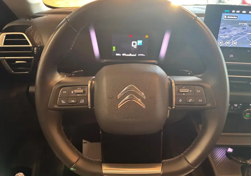Vue rapprochée du volant en cuir noir du Citroën C4 X 2024, avec commandes intégrées et tableau de bord numérique allumé.