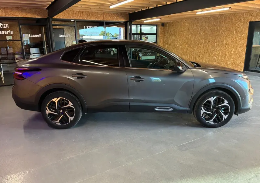 Vue de profil côté gauche d'une Citroën C4 X gris 2024 avec jantes noires et détails de carrosserie noirs.