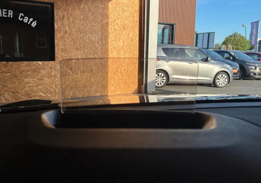 Vue depuis l'intérieur sur le tableau de bord avec tête haute, montrant une Citroën C4 X gris métallisé en stationnement côté droit.