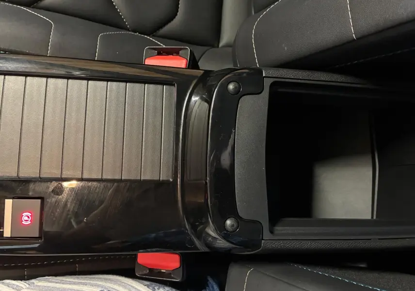 Vue plongeante sur la console centrale noire brillante de la Citroën C4 X 2024 avec accoudoir ouvert et sièges gris foncé.