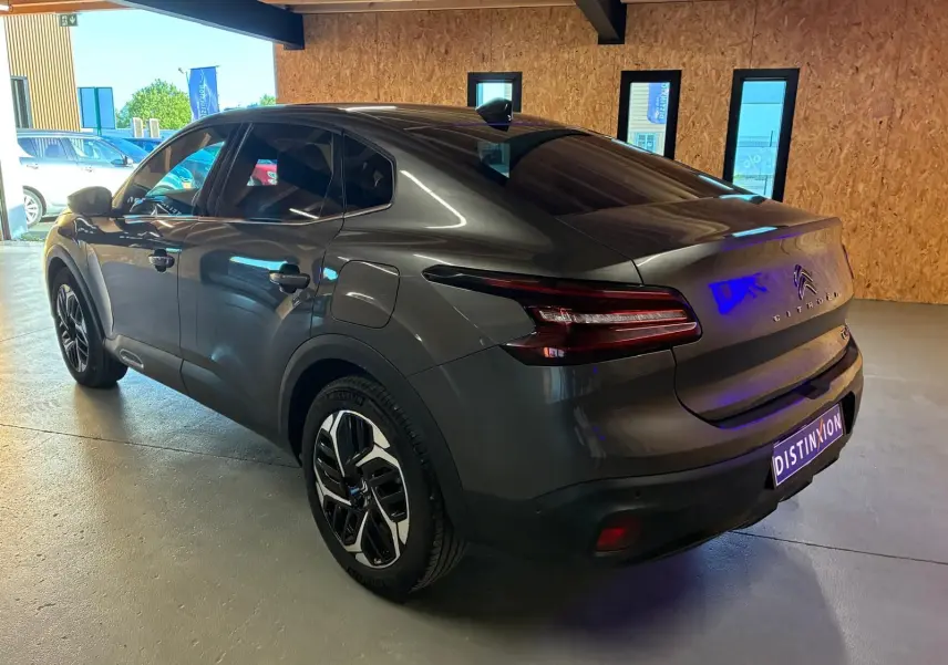 Vue 3/4 arrière droite d'une Citroën C4 X gris métallisé 2024 avec feux arrière LED et jantes bicolores.