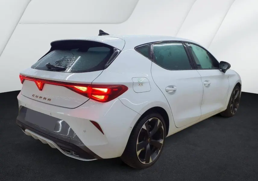 Vue 3/4 arrière droite d'une CUPRA Leon blanc Nevada avec feux arrière allumés et jantes alliage noires.