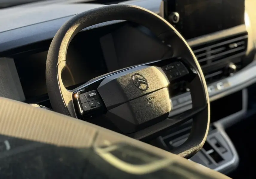 Volant noir Citroën Jumpy 2025 en gros plan avec commandes intégrées, tableau de bord et écran tactile en arrière-plan.