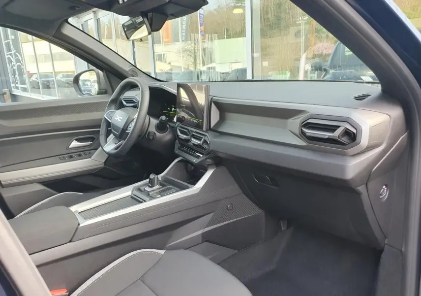Vue intérieure côté passager du Dacia Bigster bleu indigo, mettant en valeur le tableau de bord moderne et l'écran tactile central.