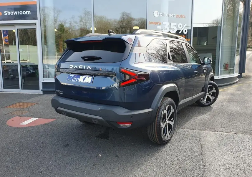 Vue 3/4 arrière droite d'un Dacia Bigster bleu indigo avec toit panoramique et jantes alliage diamantées.