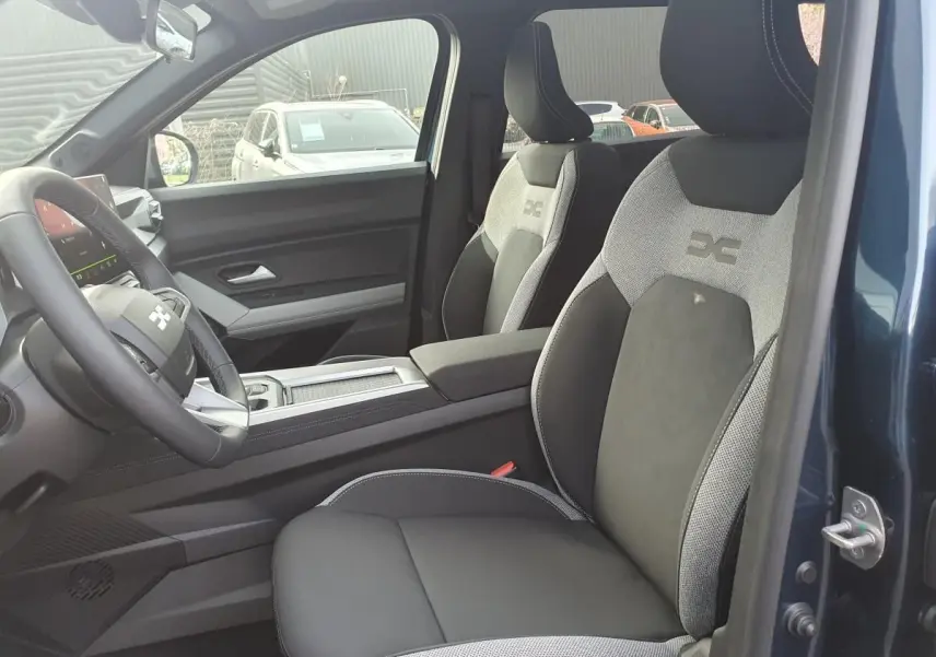 Vue intérieure côté conducteur du Dacia Bigster bleu indigo, mettant en valeur les sièges bi-matière avec logo brodé.