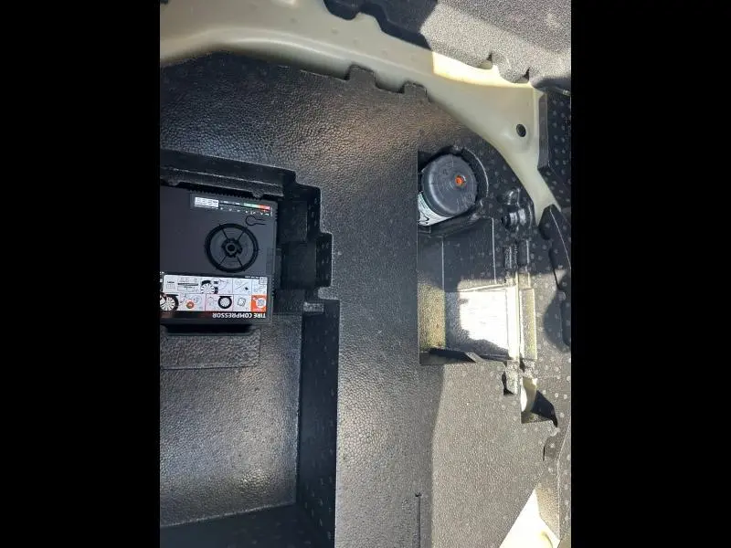 Vue rapprochée du compartiment de rangement sous le plancher de coffre d’une Citroën C3 noire 2025, montrant un compresseur d’air.