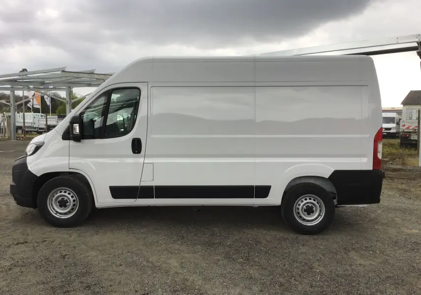 Peugeot Boxer Fourgon blanc en vue de profil côté gauche, avec carrosserie haute et longue, sur sol gravillonné.