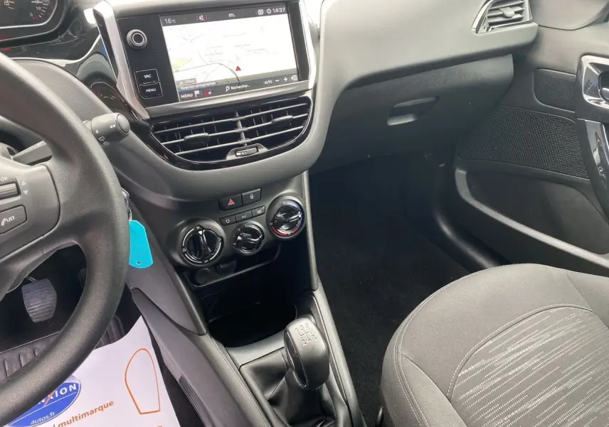 Vue intérieure côté conducteur de la Peugeot 208 Affaire noire, montrant la console centrale avec GPS et boîte manuelle.