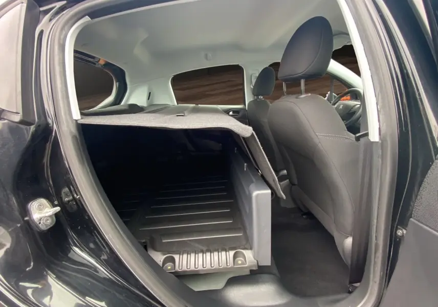 Vue intérieure côté droit arrière de la Peugeot 208 Affaire noire, montrant les sièges avant et l'espace de chargement avec tablette relevée.