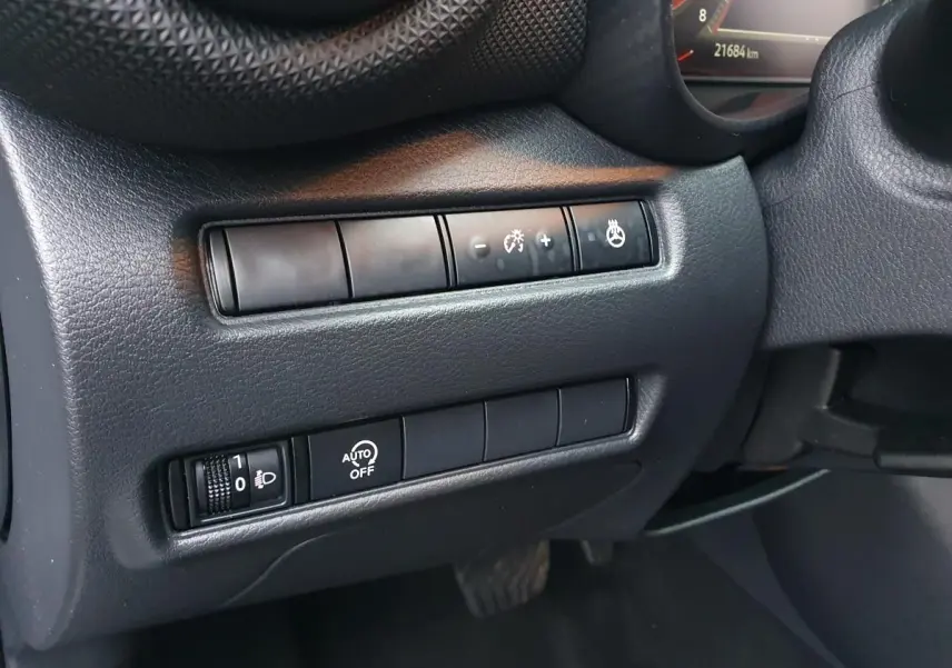 Gros plan sur les commandes de réglage d'éclairage et de chauffage du volant côté gauche du tableau de bord noir du Nissan Juke gris céramique 2025.