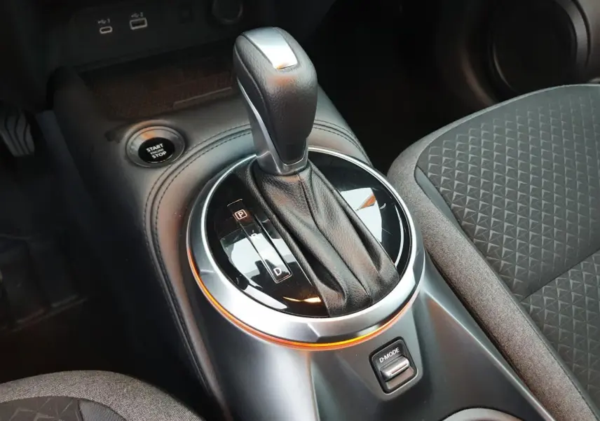 Gros plan sur la console centrale du Nissan Juke 2025 avec levier de vitesse automatique et bouton D-MODE, sièges gris à motifs.