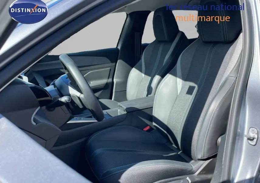 Vue intérieure côté gauche de la Peugeot 308 SW Hybrid 2025, sièges en tissu et cuir gris, volant multifonction.
