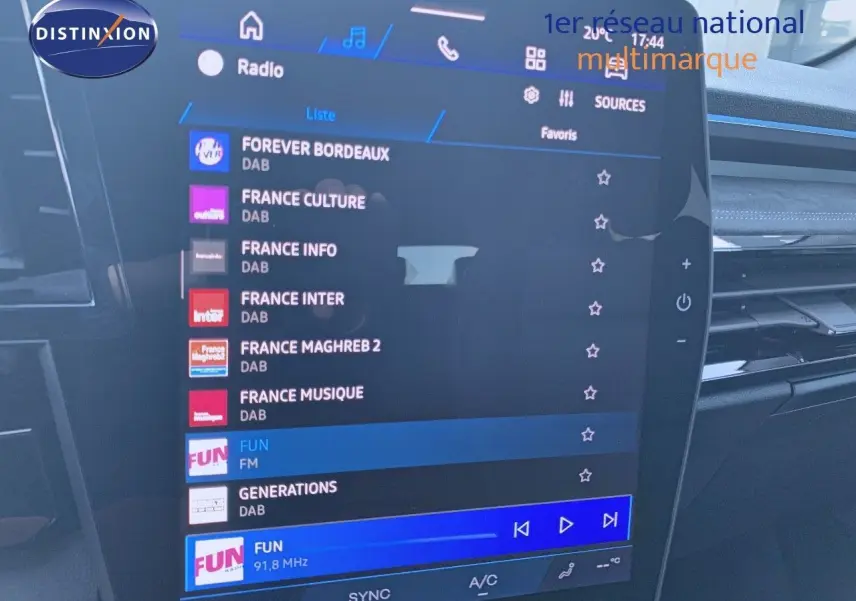 Écran tactile central du tableau de bord du Renault Austral blanc métal avec toit noir, affichant les stations radio numériques.