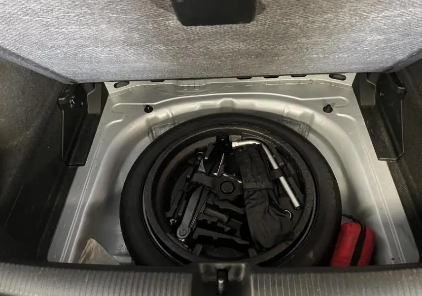 Vue du coffre ouvert de l'Audi Q2 gris montrant la roue de secours compacte et les outils de dépannage rangés.