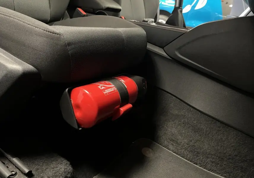 Gros plan sur l'extincteur rouge fixé sous le siège avant côté passager d'un Audi Q2 Business line gris.