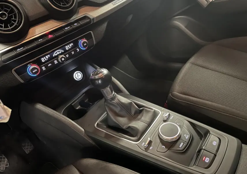 Intérieur de l'Audi Q2 2019 vu côté passager, avec levier de vitesse manuel et commandes de climatisation visibles.