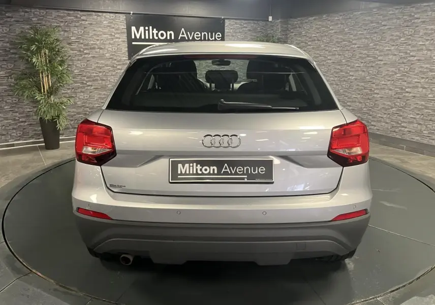 Vue arrière d'un Audi Q2 gris métallisé avec feux arrière rouges et pare-chocs inférieur noir dans un showroom.