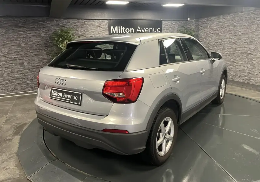 Audi Q2 gris vue 3/4 arrière droit, avec feux arrière rouges et jantes 16 pouces cinq branches.