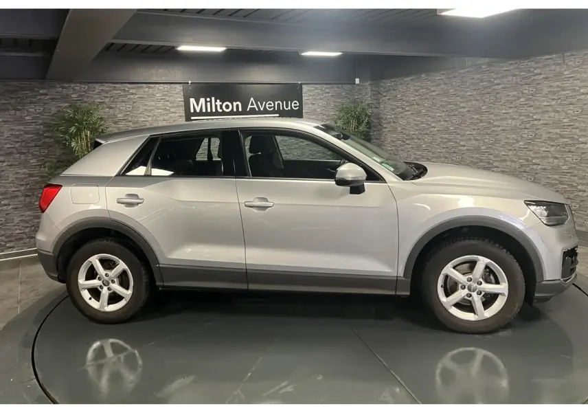 Audi Q2 gris vue de profil côté gauche dans un showroom avec jantes 5 branches et protections noires sur les bas de caisse.