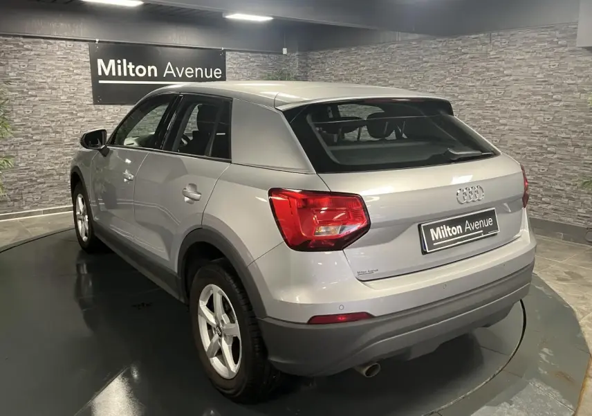 Audi Q2 gris métallisé vue 3/4 arrière droit, avec feux arrière rouges et jantes 16 pouces cinq branches.