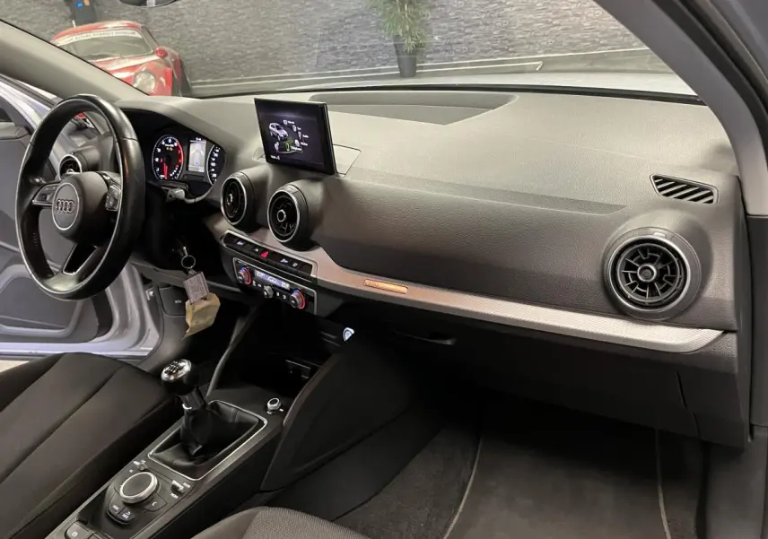 Intérieur avant droit de l'Audi Q2 gris, tableau de bord noir avec écran central et levier de vitesses manuel.