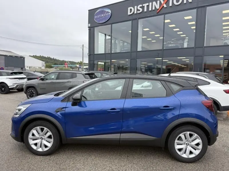 Profil côté gauche d'un Renault Captur E-Tech 145 Zen bleu métal 2022, hybride essence, devant un showroom Distinxion.