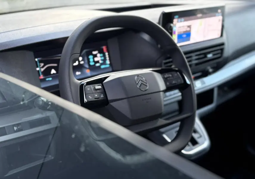 Vue rapprochée du volant Citroën Jumpy 2025 avec commandes intégrées et écran GPS tactile en arrière-plan.