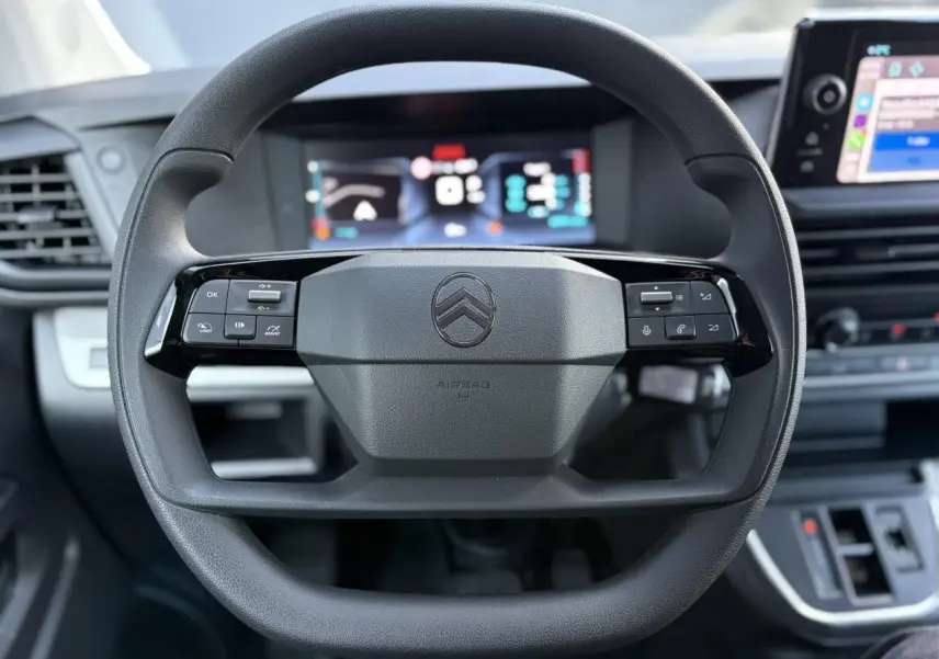Vue rapprochée du volant noir du Citroën Jumpy XL 2025 avec commandes intégrées et tableau de bord numérique flou.