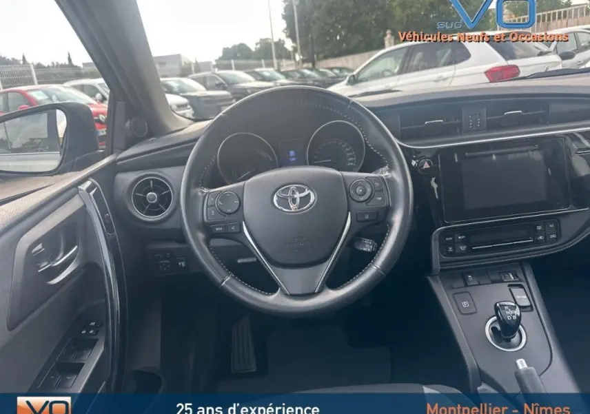 Vue intérieure du poste de conduite de la Toyota Auris Business Hybride 2016, volant multifonctions et écran tactile central visibles.