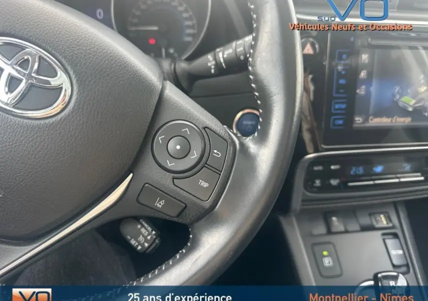 Gros plan sur le volant multifonctions en cuir noir de la Toyota Auris Business Hybride 2016 avec tableau de bord et écran tactile.