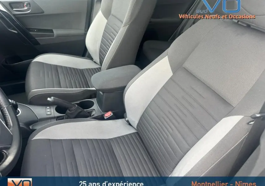 Vue intérieure des sièges avant gris clair et foncé de la Toyota Auris Business Hybride 2016 avec accoudoir central.